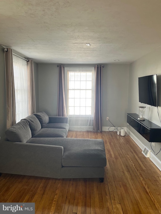 living room with hardwood / wood-style flooring, baseboards, visible vents, and a textured ceiling