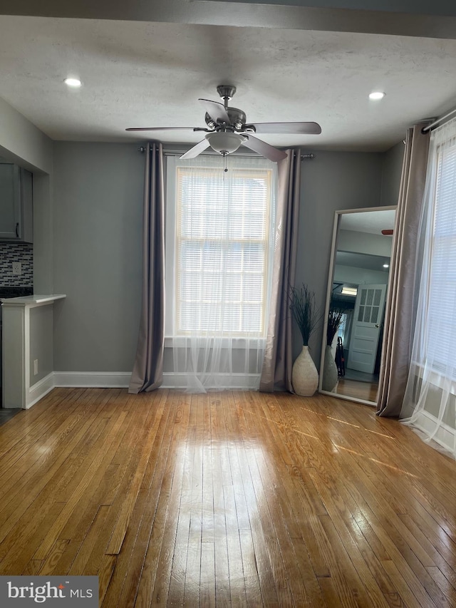 unfurnished dining area featuring wood-type flooring, baseboards, ceiling fan, and a wealth of natural light