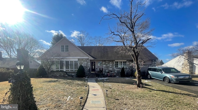 view of front of home featuring aphalt driveway, a shingled roof, a garage, stone siding, and a front lawn