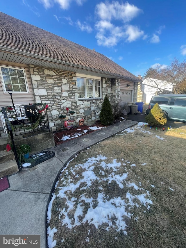 view of home's exterior featuring a garage, stone siding, and a shingled roof