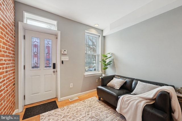 entryway featuring brick wall, light wood-style flooring, visible vents, and baseboards