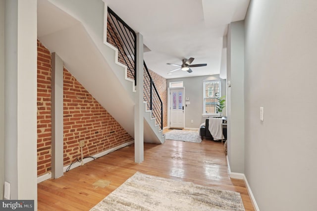 entrance foyer with brick wall, baseboards, stairway, and light wood finished floors