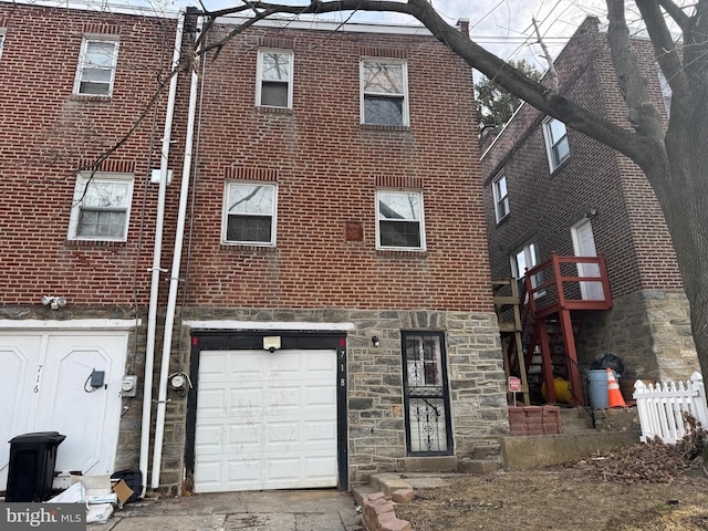 view of front of property featuring a garage, stone siding, fence, and brick siding