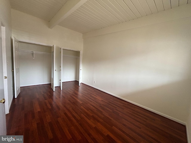 unfurnished bedroom featuring dark wood-style floors, multiple closets, wooden ceiling, beamed ceiling, and baseboards