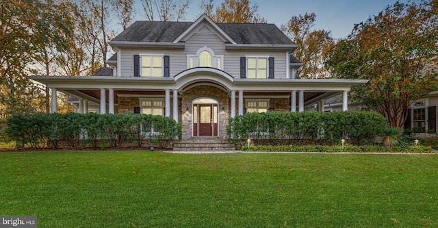 view of front of home featuring a porch, a front yard, stone siding, and a shingled roof