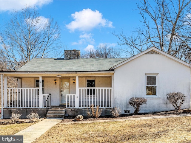 ranch-style home with covered porch, a shingled roof, a chimney, and stucco siding