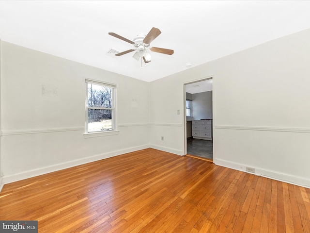 empty room with visible vents, light wood finished floors, a ceiling fan, and baseboards