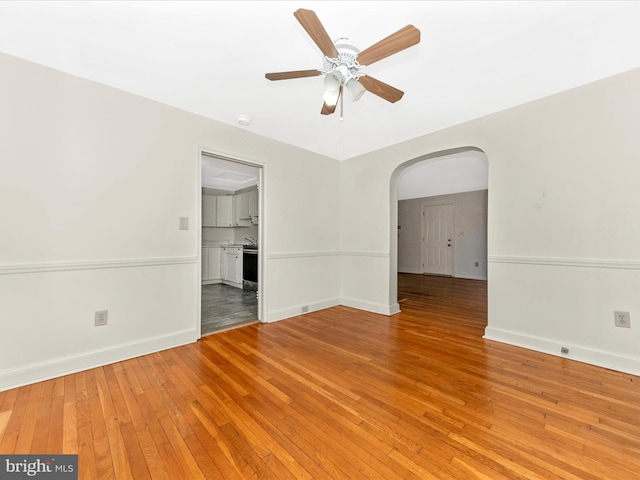 unfurnished room featuring light wood-style floors, arched walkways, and baseboards