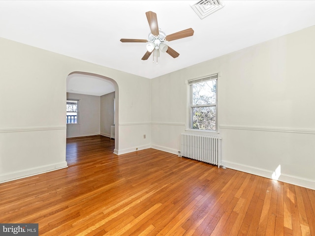 unfurnished room with arched walkways, a healthy amount of sunlight, light wood-type flooring, and radiator