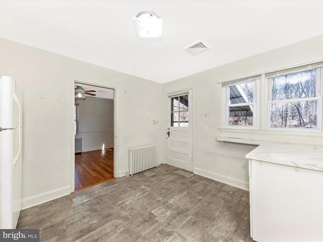 unfurnished dining area with baseboards, radiator heating unit, visible vents, and wood finished floors