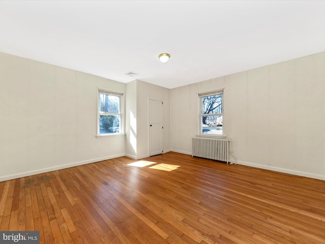 spare room with baseboards, visible vents, hardwood / wood-style floors, and radiator heating unit