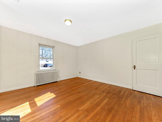 spare room with radiator heating unit, light wood-type flooring, and baseboards