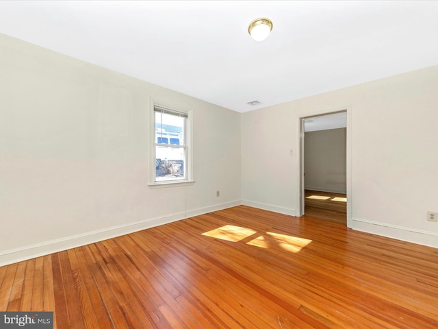 empty room with light wood-type flooring, visible vents, and baseboards