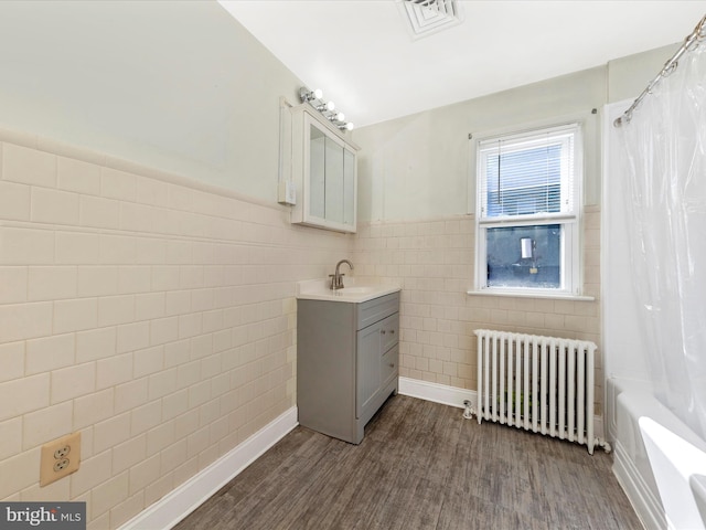 bathroom with a wainscoted wall, tile walls, radiator heating unit, vanity, and wood finished floors