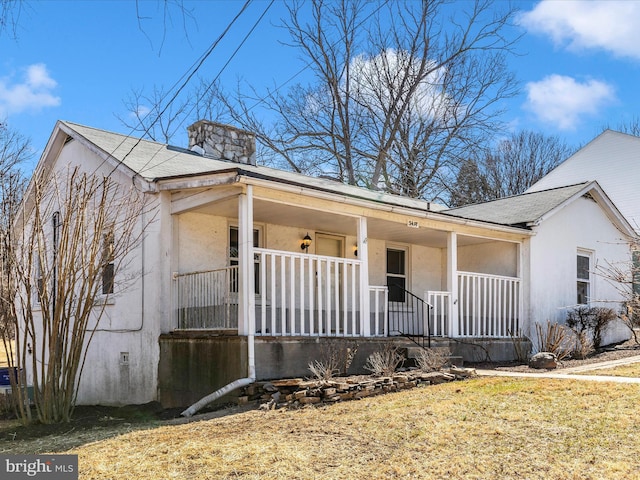 view of front facade with covered porch, a chimney, and stucco siding