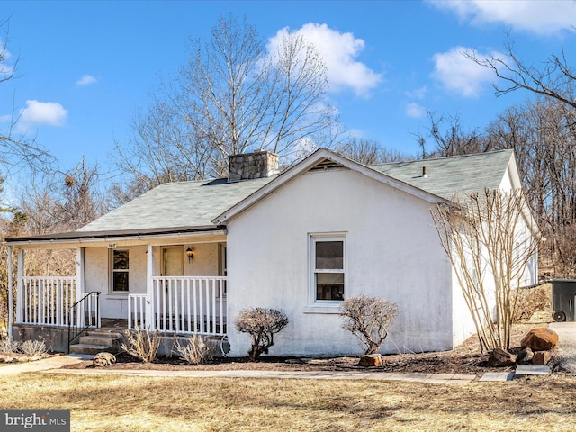 ranch-style home with covered porch, roof with shingles, a chimney, and stucco siding