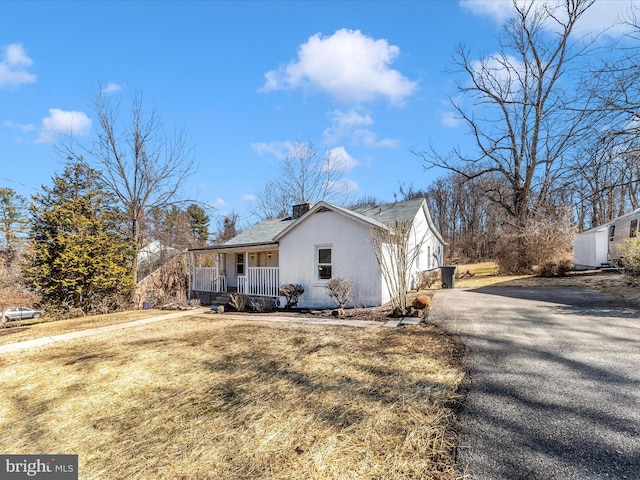 view of side of home featuring aphalt driveway, covered porch, a yard, and a chimney