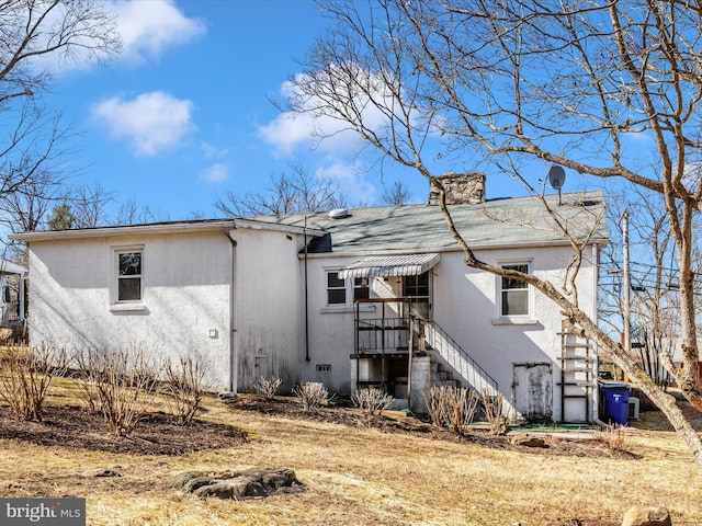 back of property featuring stairs, a chimney, and stucco siding