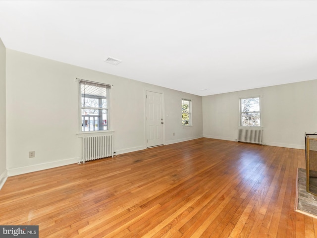 unfurnished living room featuring radiator, light wood finished floors, baseboards, and visible vents