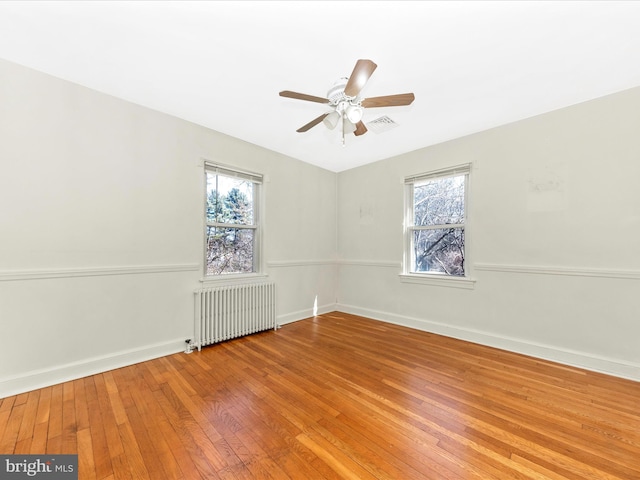 unfurnished room featuring radiator, visible vents, a ceiling fan, baseboards, and hardwood / wood-style flooring