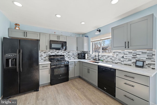 kitchen with light wood-style flooring, a sink, light countertops, gray cabinets, and black appliances