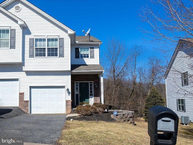 view of front facade with aphalt driveway, a garage, central AC, brick siding, and a front yard