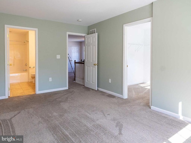 unfurnished bedroom featuring baseboards, visible vents, ensuite bath, a spacious closet, and carpet floors