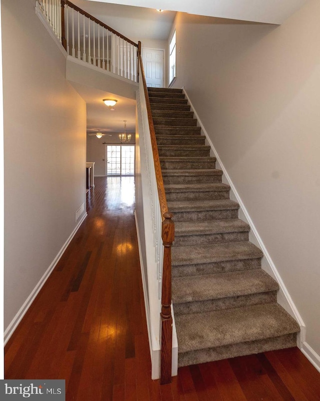 stairs featuring an inviting chandelier, wood-type flooring, visible vents, and baseboards