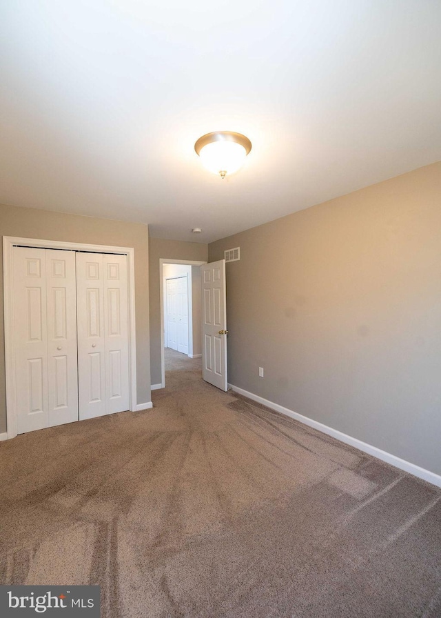 unfurnished bedroom with carpet floors, visible vents, baseboards, and a closet