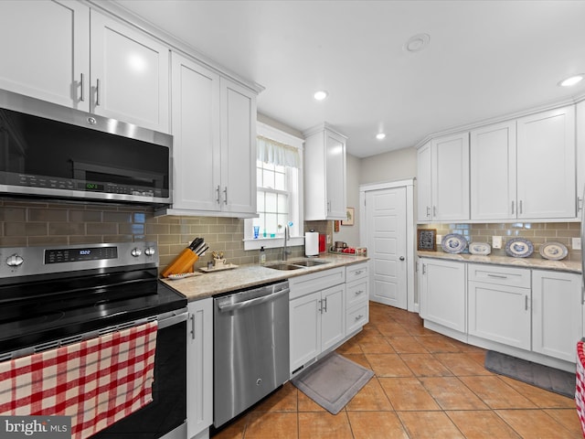 kitchen featuring light tile patterned floors, a sink, appliances with stainless steel finishes, white cabinetry, and backsplash