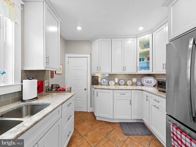 kitchen featuring a sink, backsplash, freestanding refrigerator, white cabinets, and glass insert cabinets