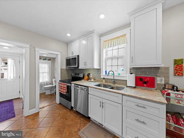 kitchen with light tile patterned floors, a sink, stainless steel appliances, white cabinets, and tasteful backsplash