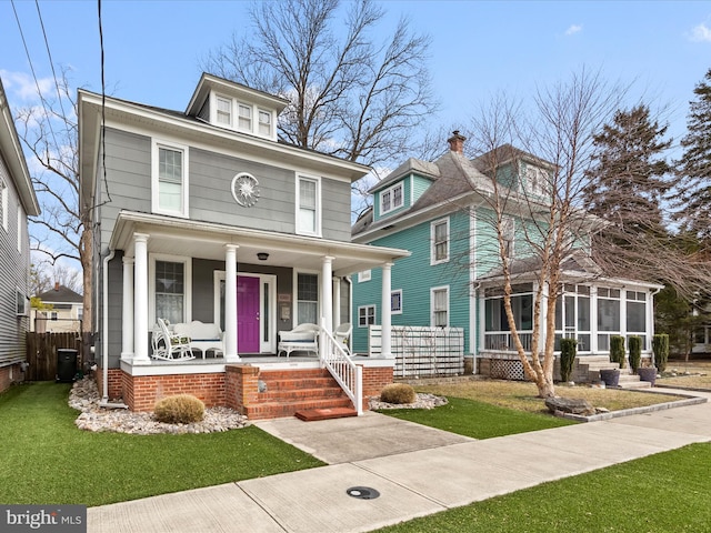 american foursquare style home featuring a porch, a front lawn, and a sunroom