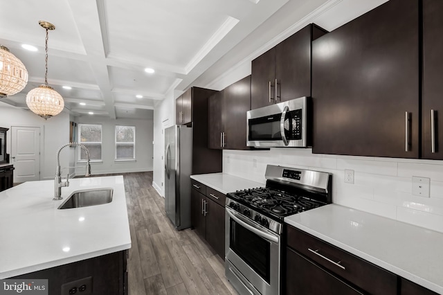 kitchen with coffered ceiling, appliances with stainless steel finishes, light countertops, and a sink