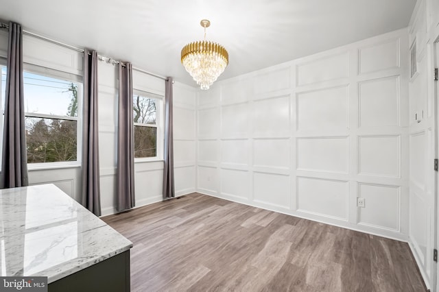 unfurnished dining area featuring a decorative wall, light wood-style flooring, and an inviting chandelier