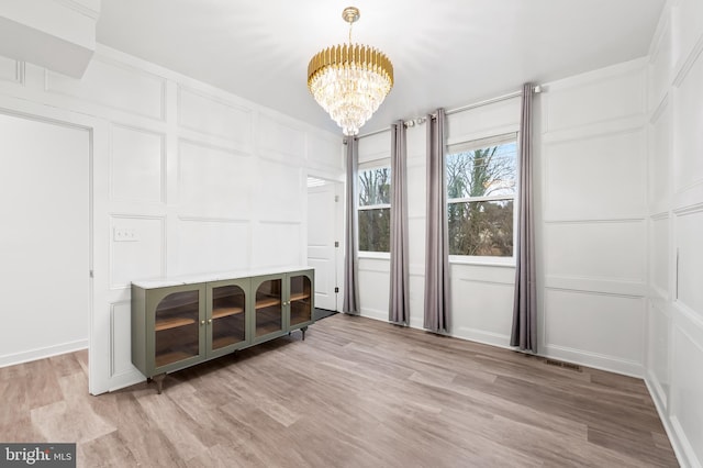 interior space featuring a chandelier, light wood finished floors, visible vents, and a decorative wall