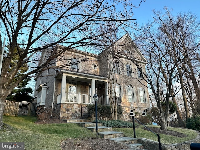 traditional-style home featuring covered porch, brick siding, stone siding, a gate, and a front lawn