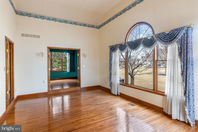 unfurnished dining area featuring a towering ceiling, baseboards, visible vents, light wood finished floors, and wallpapered walls