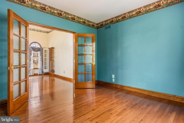 unfurnished room with french doors, visible vents, baseboards, and hardwood / wood-style floors