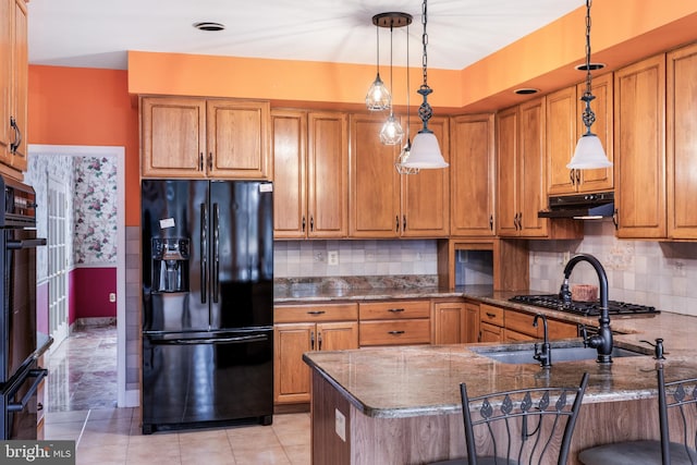 kitchen featuring brown cabinets, black appliances, under cabinet range hood, and decorative backsplash