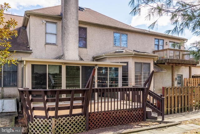 back of house with a deck, a shingled roof, fence, a sunroom, and stucco siding