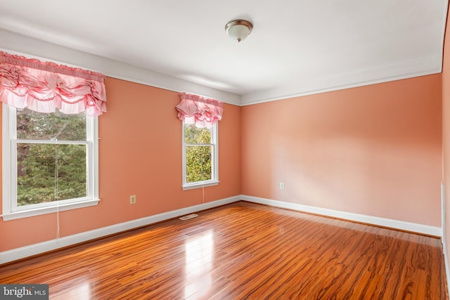 empty room featuring wood finished floors, visible vents, and baseboards