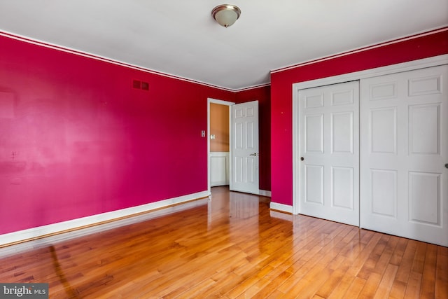 unfurnished bedroom featuring baseboards, a closet, visible vents, and hardwood / wood-style floors