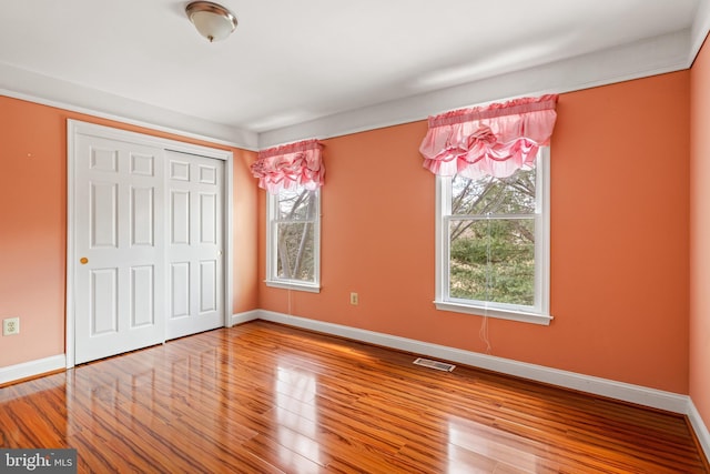 unfurnished bedroom featuring a closet, visible vents, baseboards, and wood finished floors