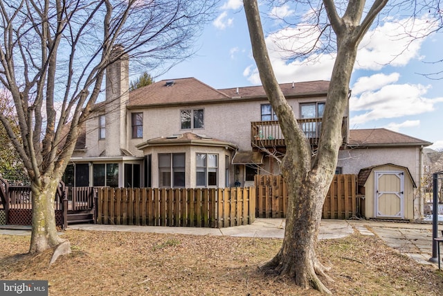 back of property featuring an outbuilding, stucco siding, fence, a shed, and a wooden deck