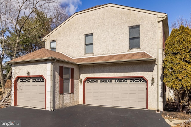 view of front facade featuring an attached garage, a shingled roof, aphalt driveway, and stucco siding