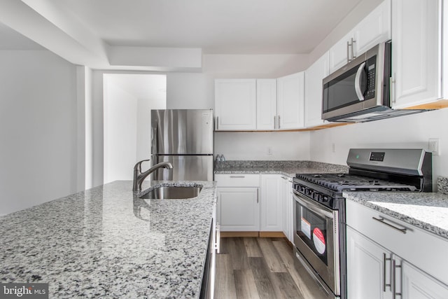 kitchen featuring light stone counters, dark wood-style floors, appliances with stainless steel finishes, white cabinetry, and a sink