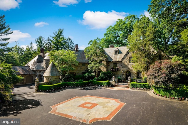 view of front facade with a high end roof, stone siding, and driveway