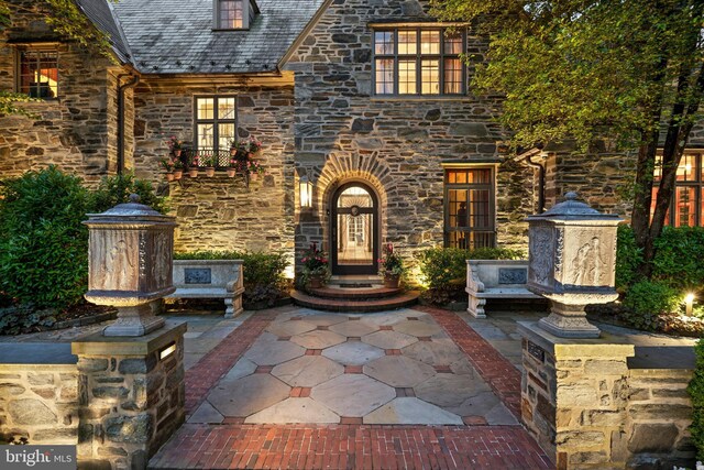 entrance to property featuring stone siding, a patio, and a high end roof