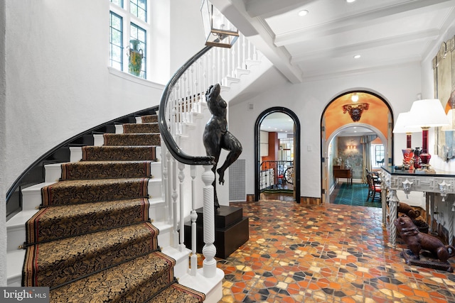 foyer entrance with arched walkways, beam ceiling, a healthy amount of sunlight, and stairway